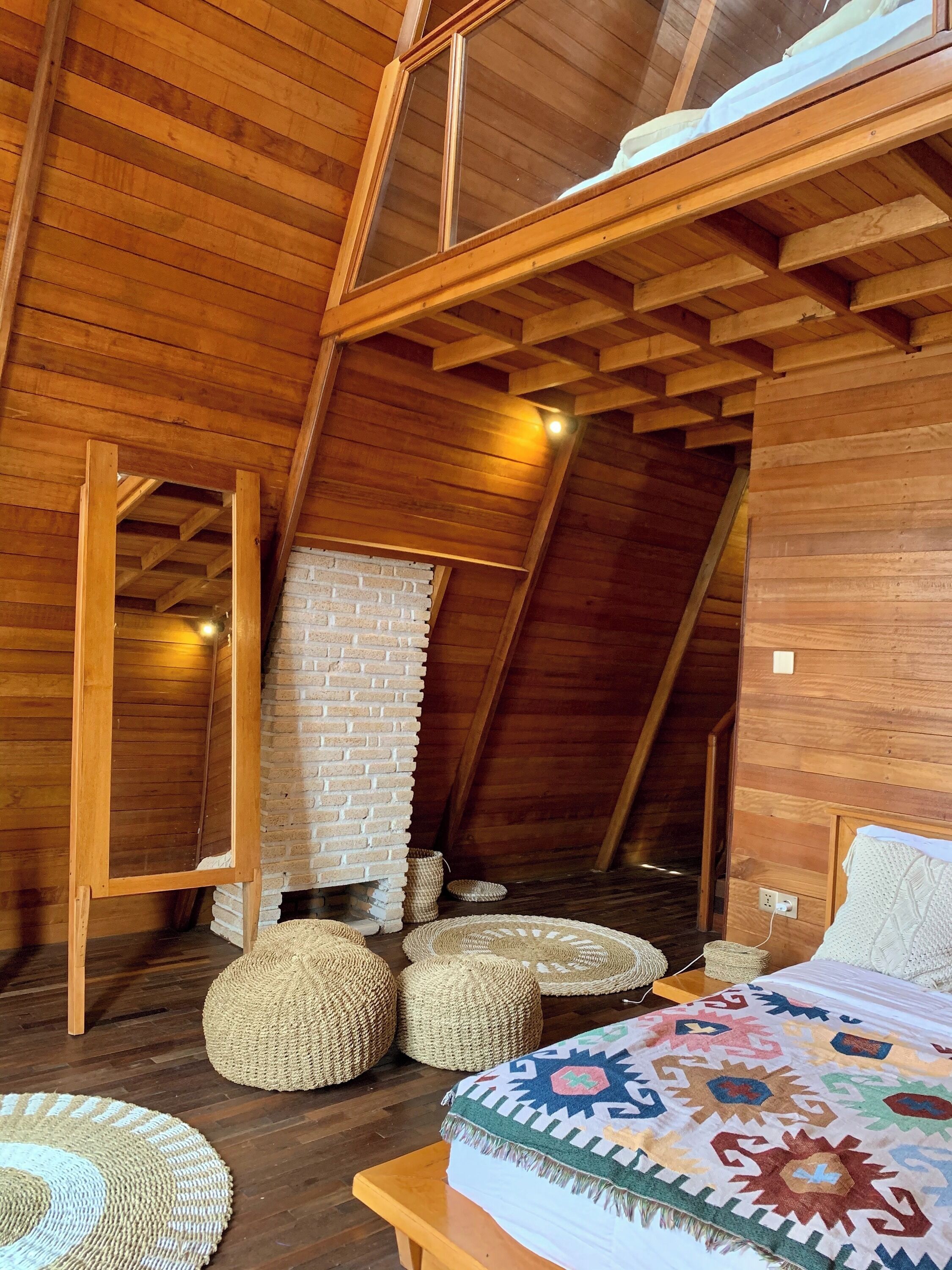 A cozy attic bedroom with wooden beams, a brick wall, and a bed with a colorful blanket.