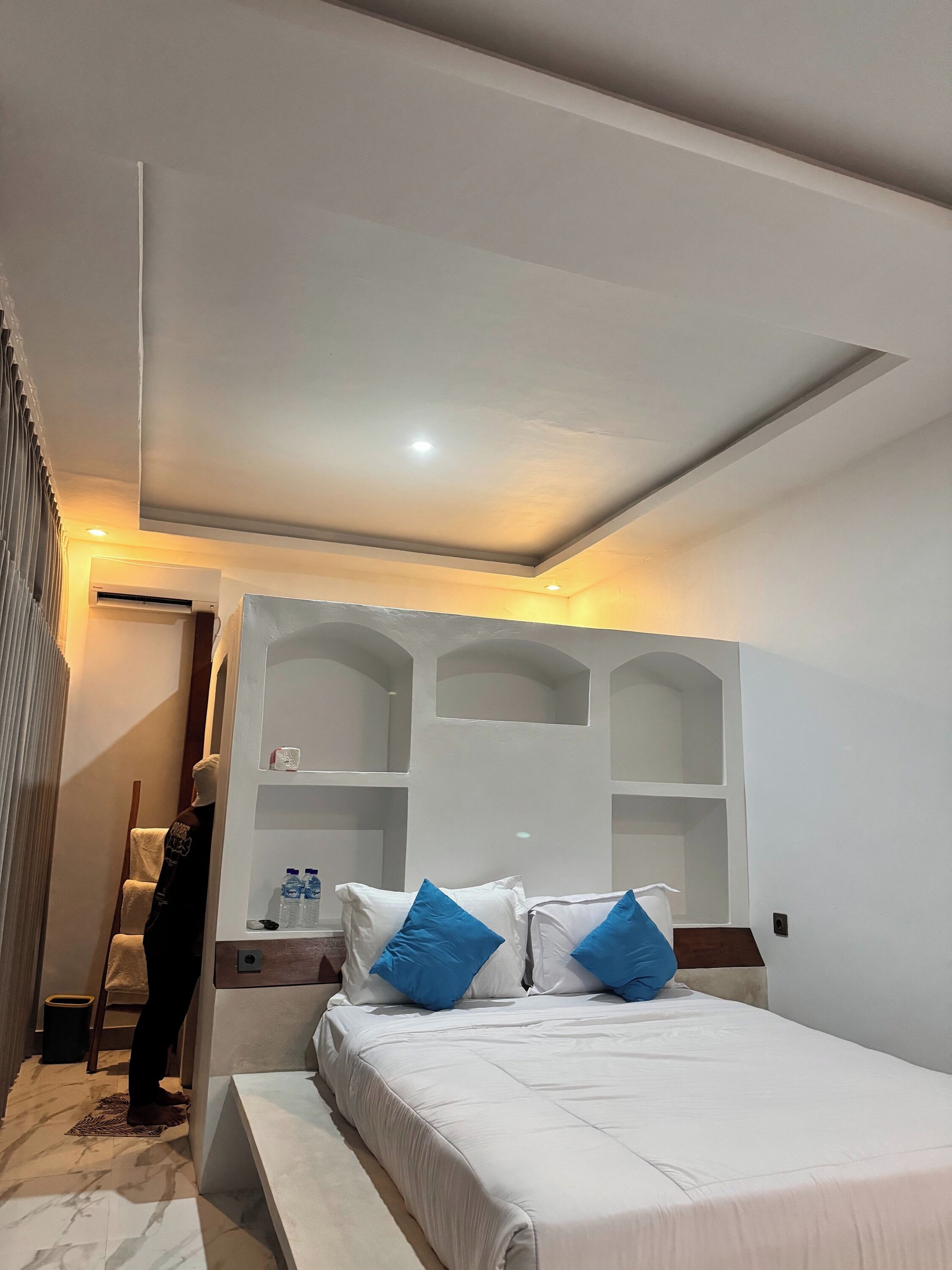 A modern hotel room with a large bed, built-in shelving, and a small table.