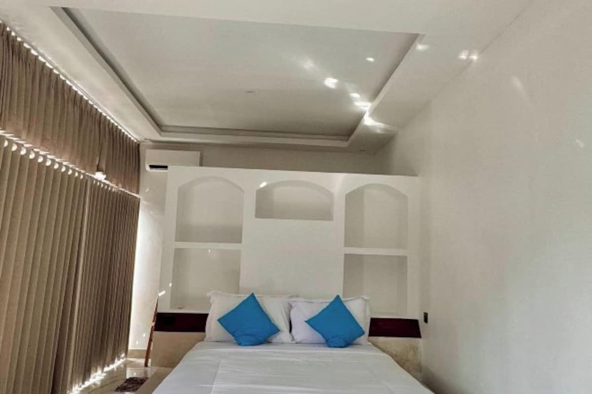 Una habitación de hotel con una cama grande, un cabecero con estantes integrados e iluminación empotrada en el techo.