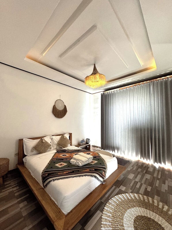 A modern bedroom with a large bed, a hanging light fixture, a woven rug, and a view of the outdoors through a window with curtains. - Volcano Side Kintamani Bali (Kintamani)