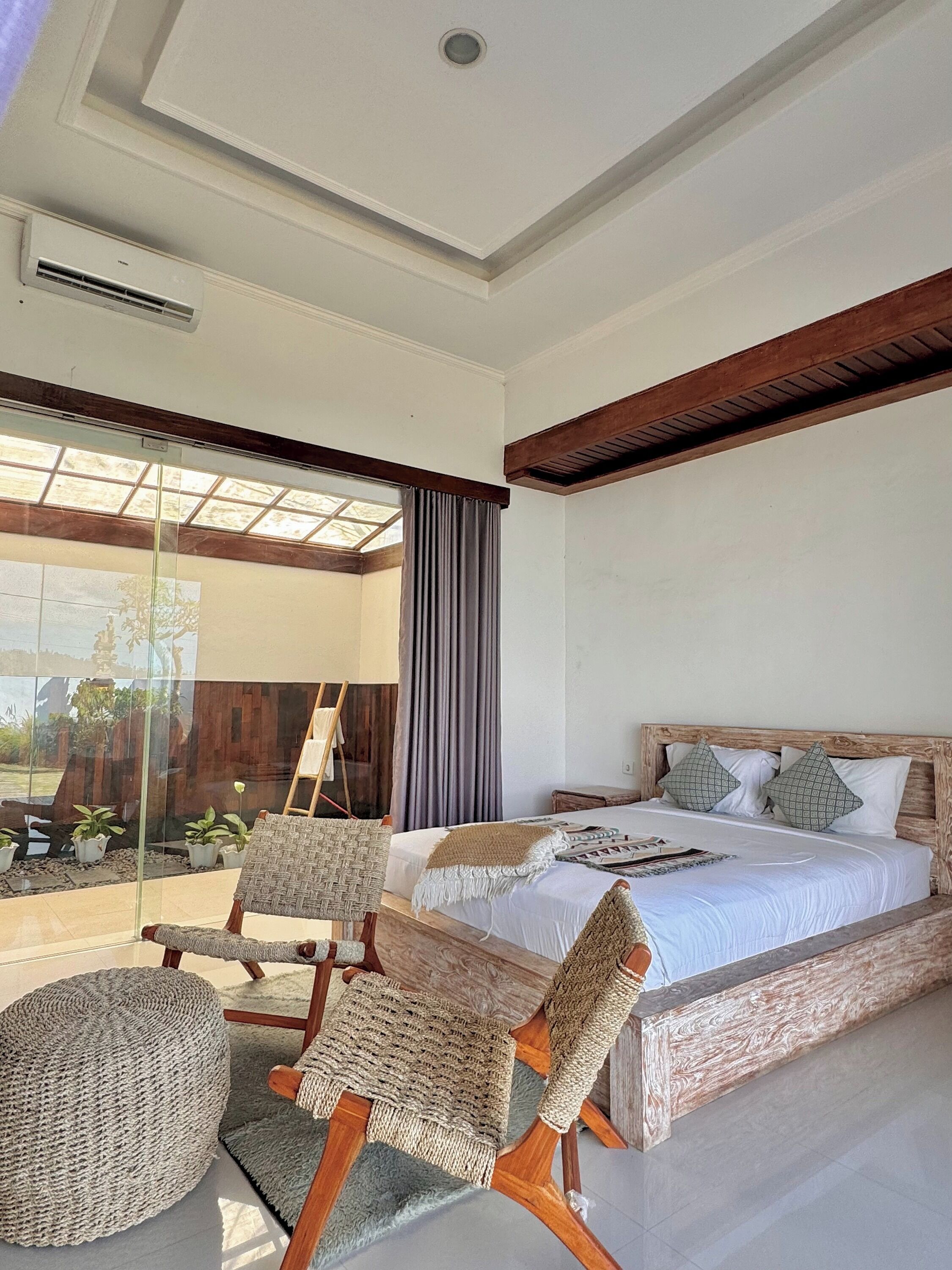 A bedroom with a large bed, two chairs, a glass partition, and a skylight.