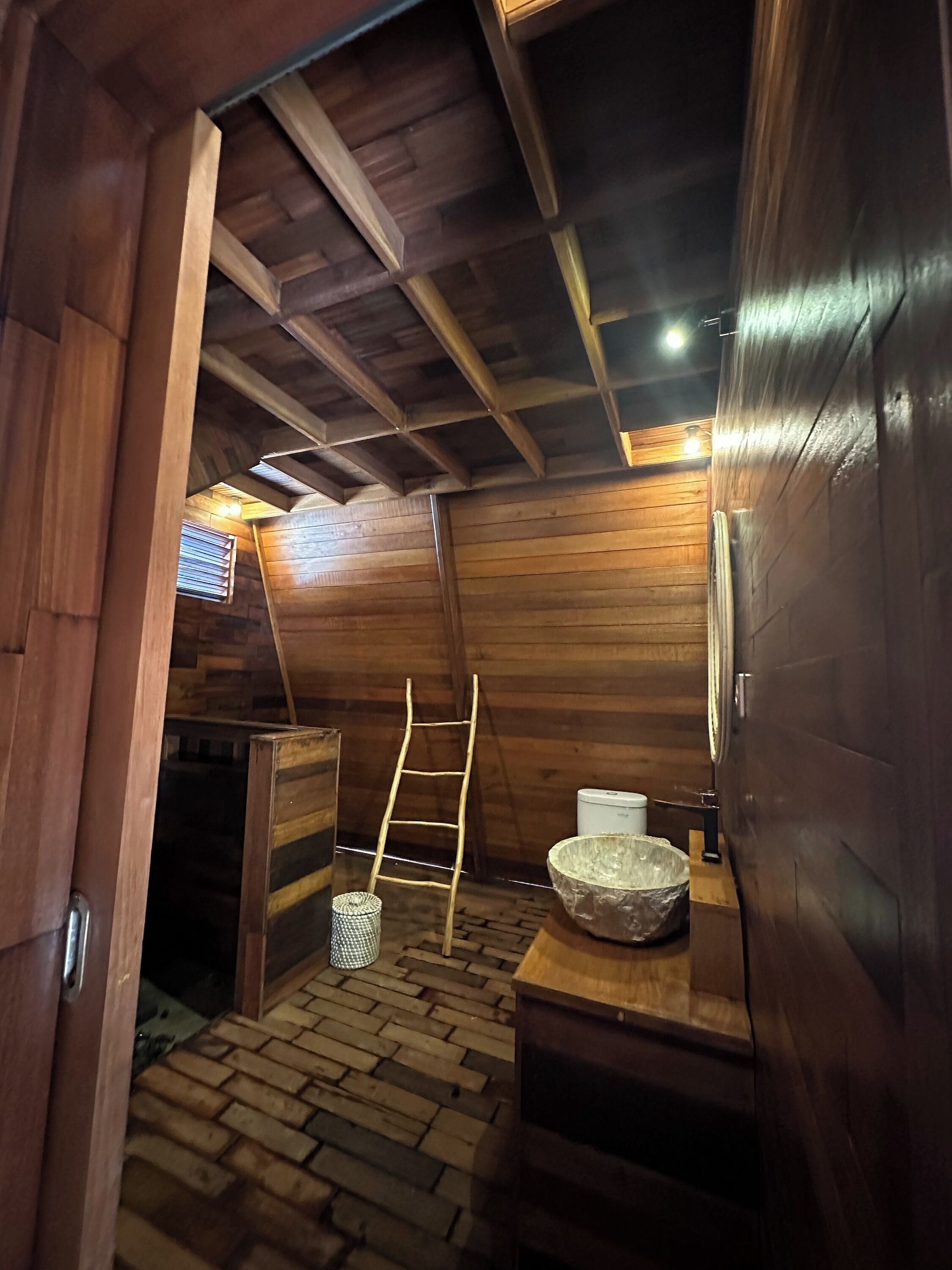 A wooden interior with a ladder, a white basin, and a brick floor.