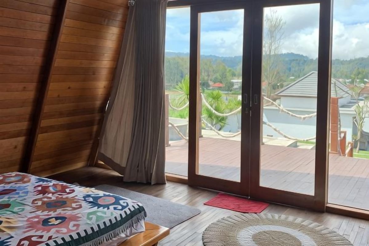 Una habitación con una cama, un ventanal corredero a una terraza y vistas a una casa y el paisaje.
