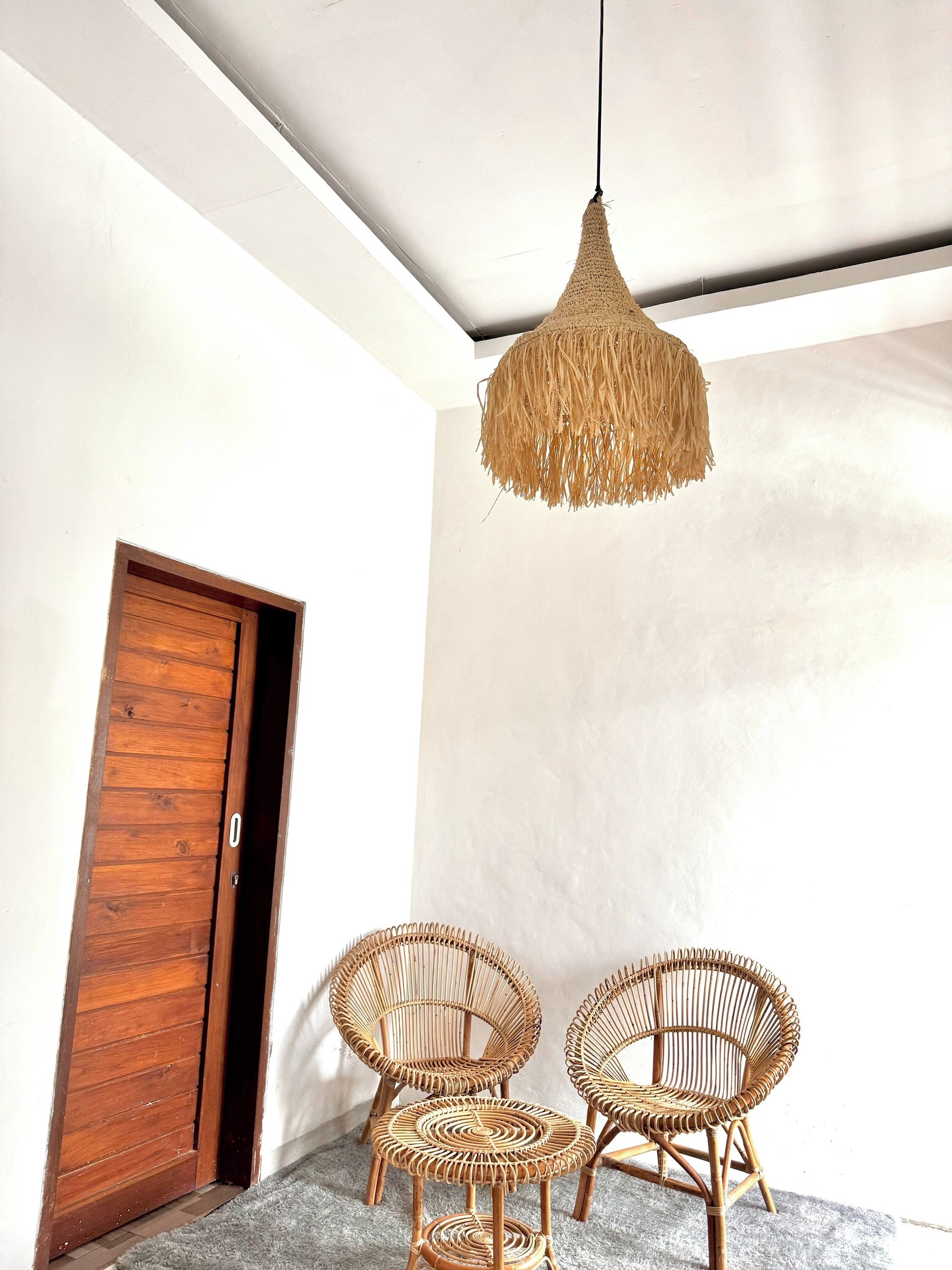 A room with a wooden door, a woven pendant light, and two wicker chairs.
