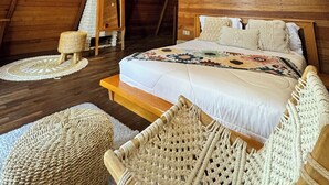 A cozy attic bedroom with a sloped ceiling, wooden beams, a bed with a patterned blanket, and a hanging light fixture. - Volcano Side Kintamani Bali (Kintamani)