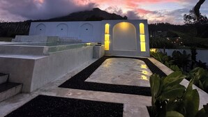 A rooftop terrace with a white wall featuring a large arched doorway and a small window, surrounded by plants and a black gravel pathway. - Volcano Side Kintamani Bali (Kintamani)