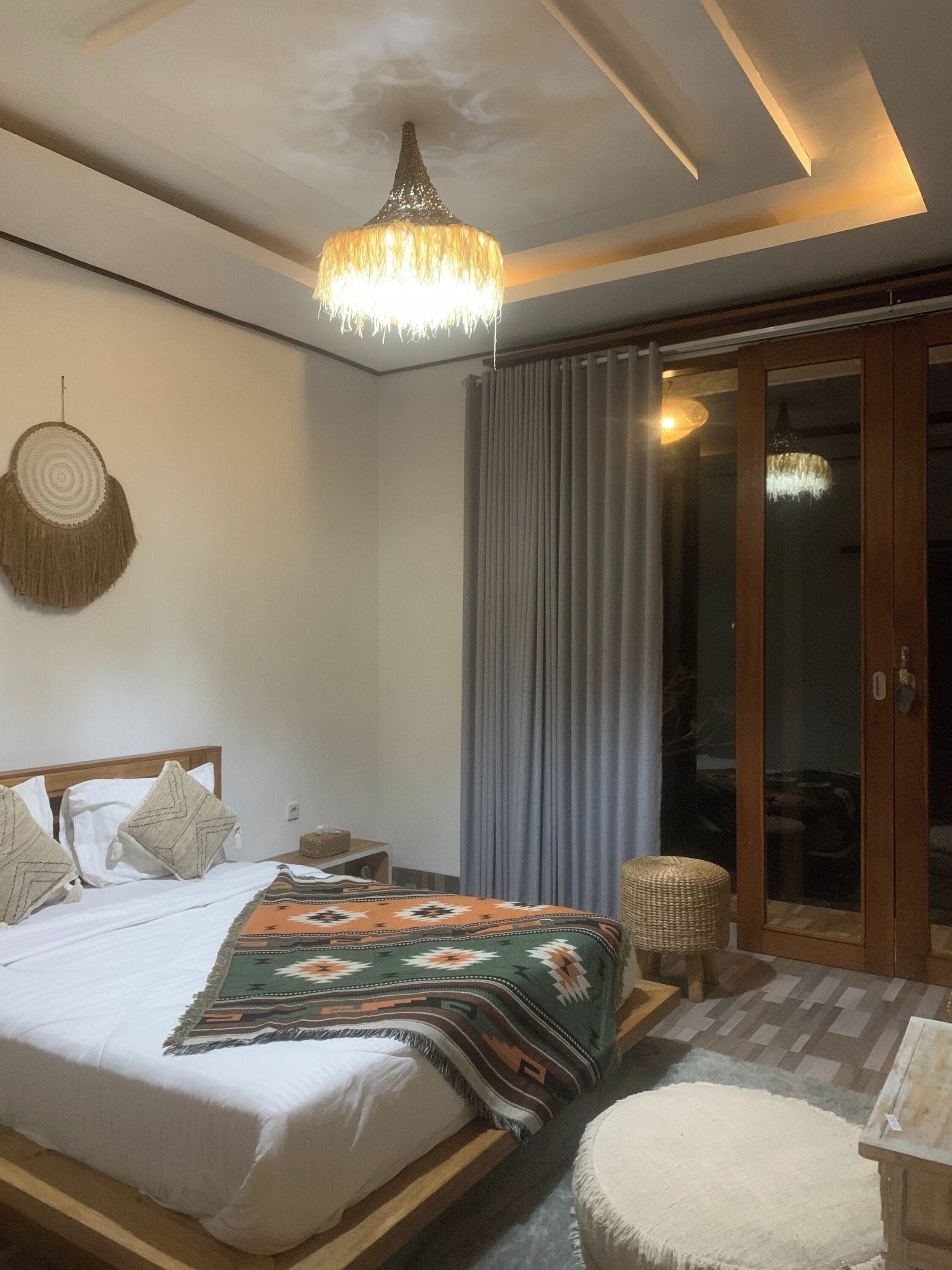 Un dormitorio con una cama, una lámpara colgante, un tapiz de pared tejido y vistas a través de un ventanal.