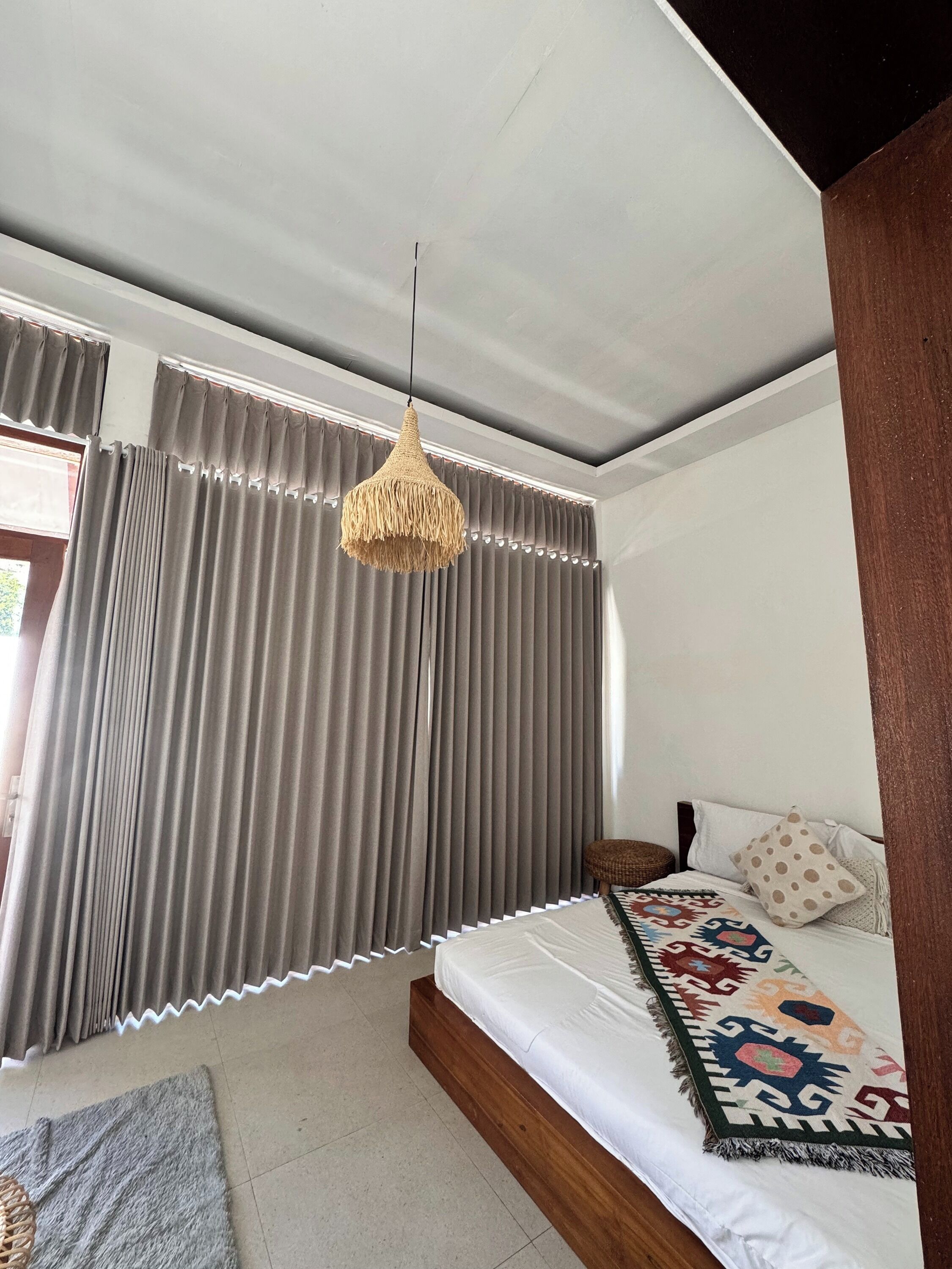 A bedroom with a bed, curtains, a hanging light fixture, and a window.