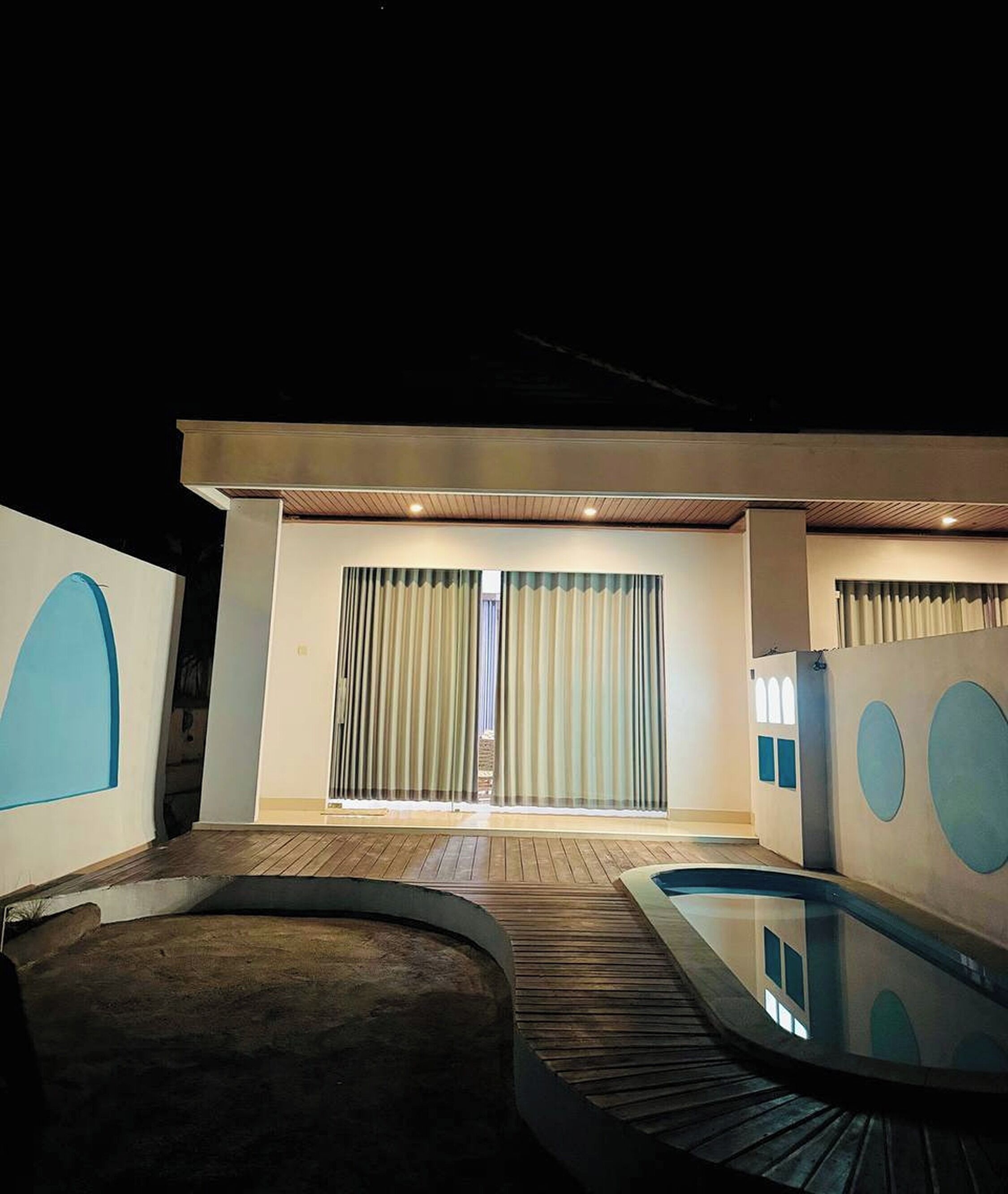 A modern interior with a pool, wooden flooring, and large windows with curtains.