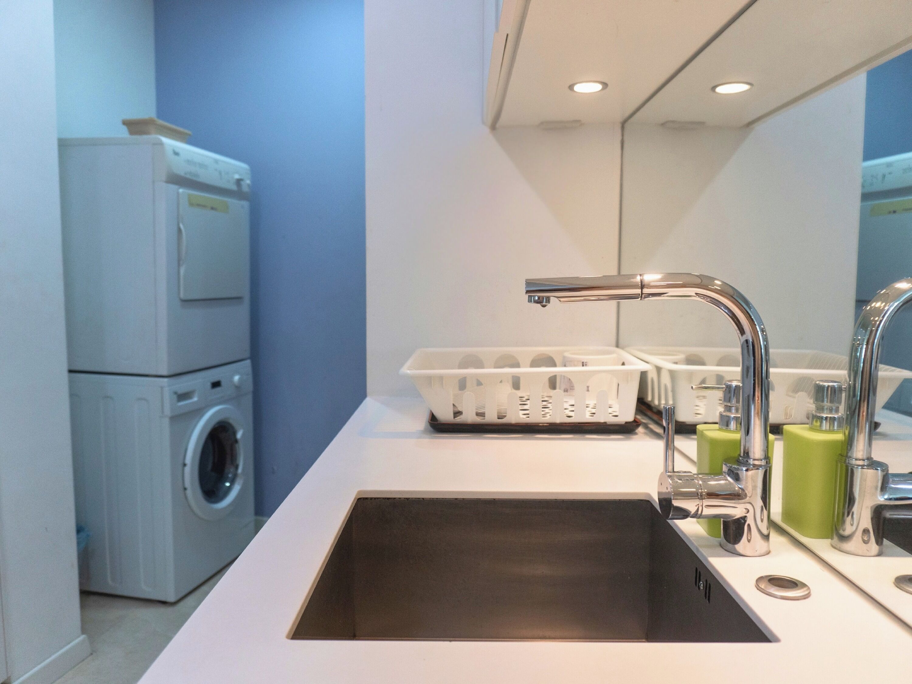 Un espace buanderie compact comprenant un lave-linge, un évier et un étendoir.