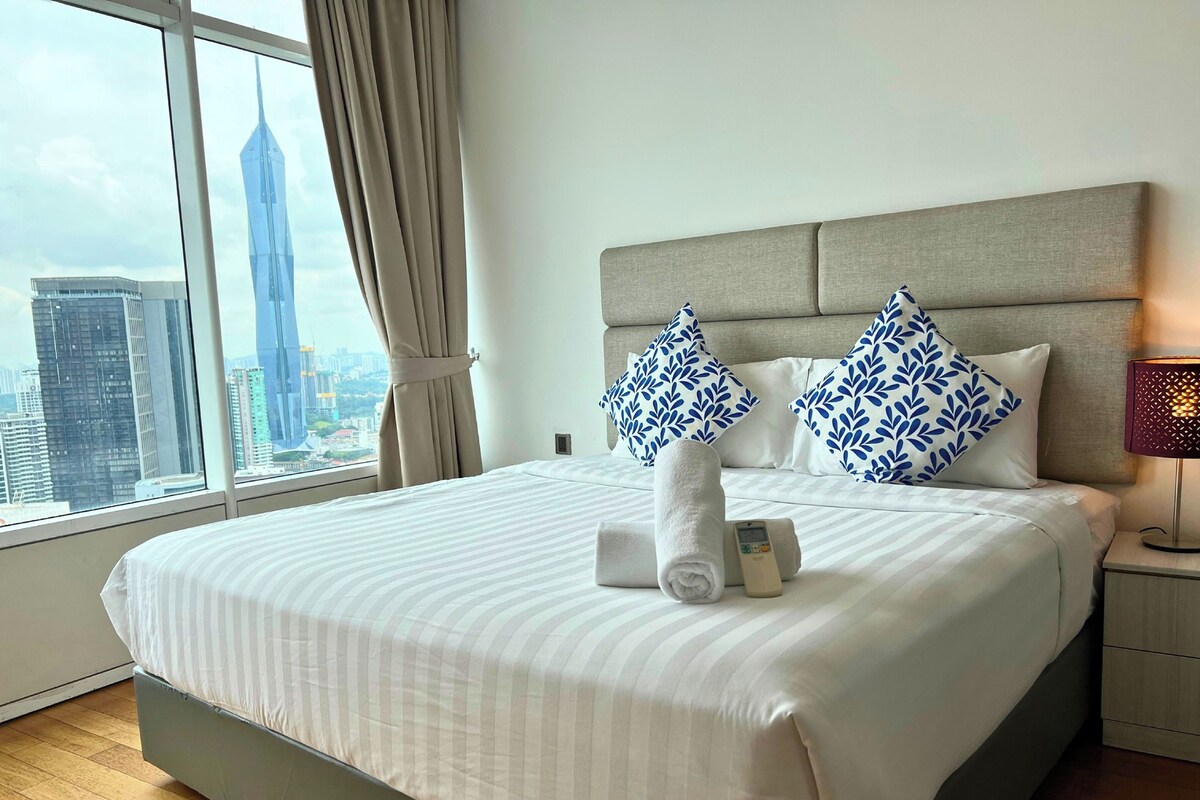 Una camera d'albergo con un letto grande, un comodino, una lampada e vista sulla città attraverso una finestra.