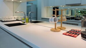 Une cuisine moderne avec un plan de travail blanc, deux éviers, un porte-tasses en bois et un récipient en verre contenant des sachets rouges.