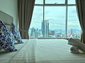 A hotel room with a large window offering a city view, a neatly made bed with striped bedding, and decorative pillows. - Vortex Apartments Kuala Lumpur (Kuala Lumpur)