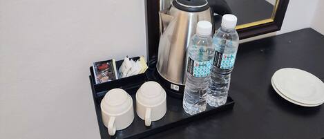 A coffee station with two white cups, two water bottles, a coffee pot, and a tray with magazines and a small box.