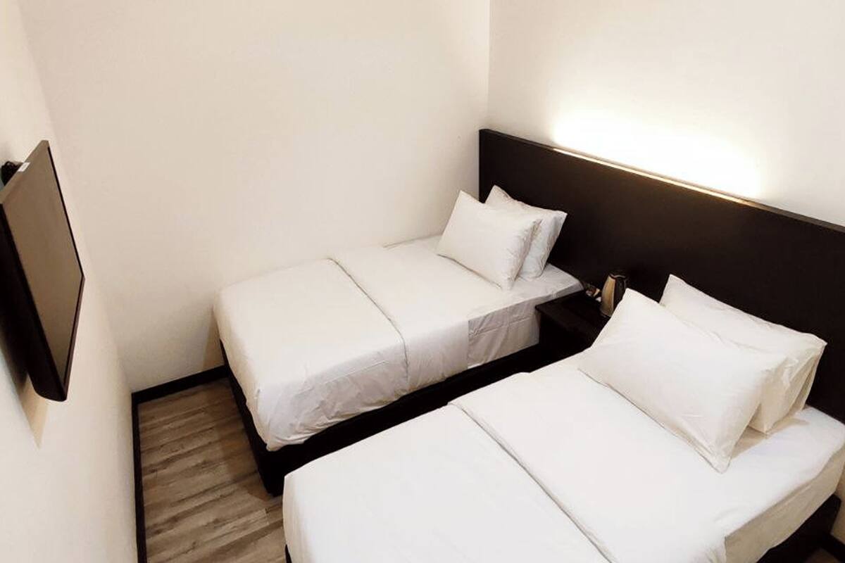 A hotel room with two beds, a flat-screen TV mounted on the wall, and a wooden floor.