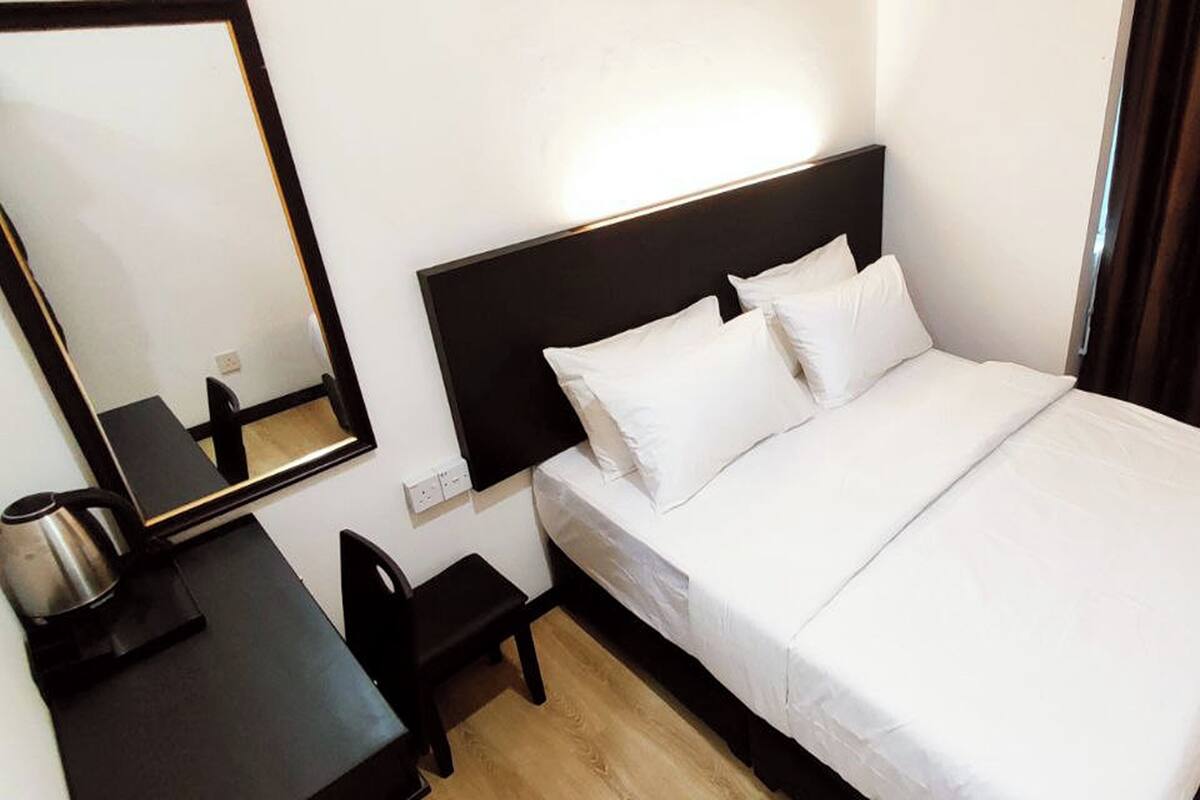 A hotel room with a bed, a desk, a chair, a mirror, and a window with curtains.