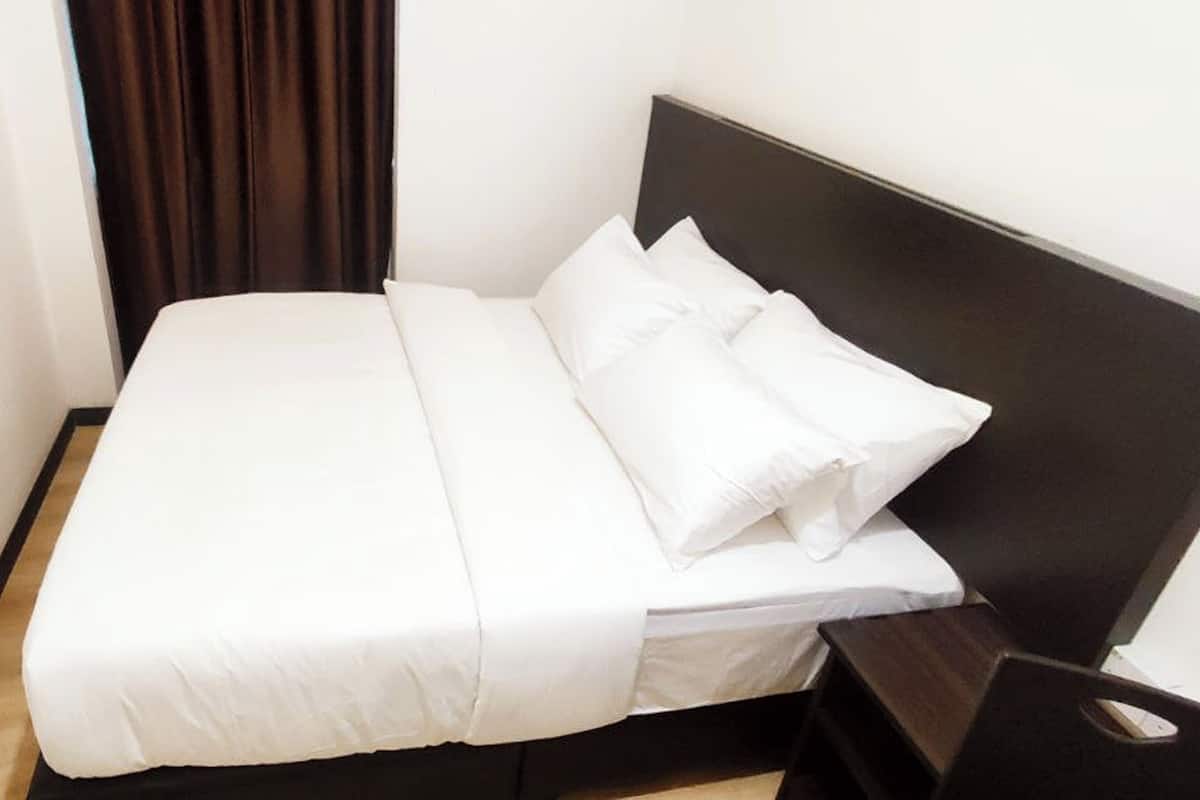 A neatly made bed with white linens and pillows, a dark headboard, and a wooden nightstand with a drawer.