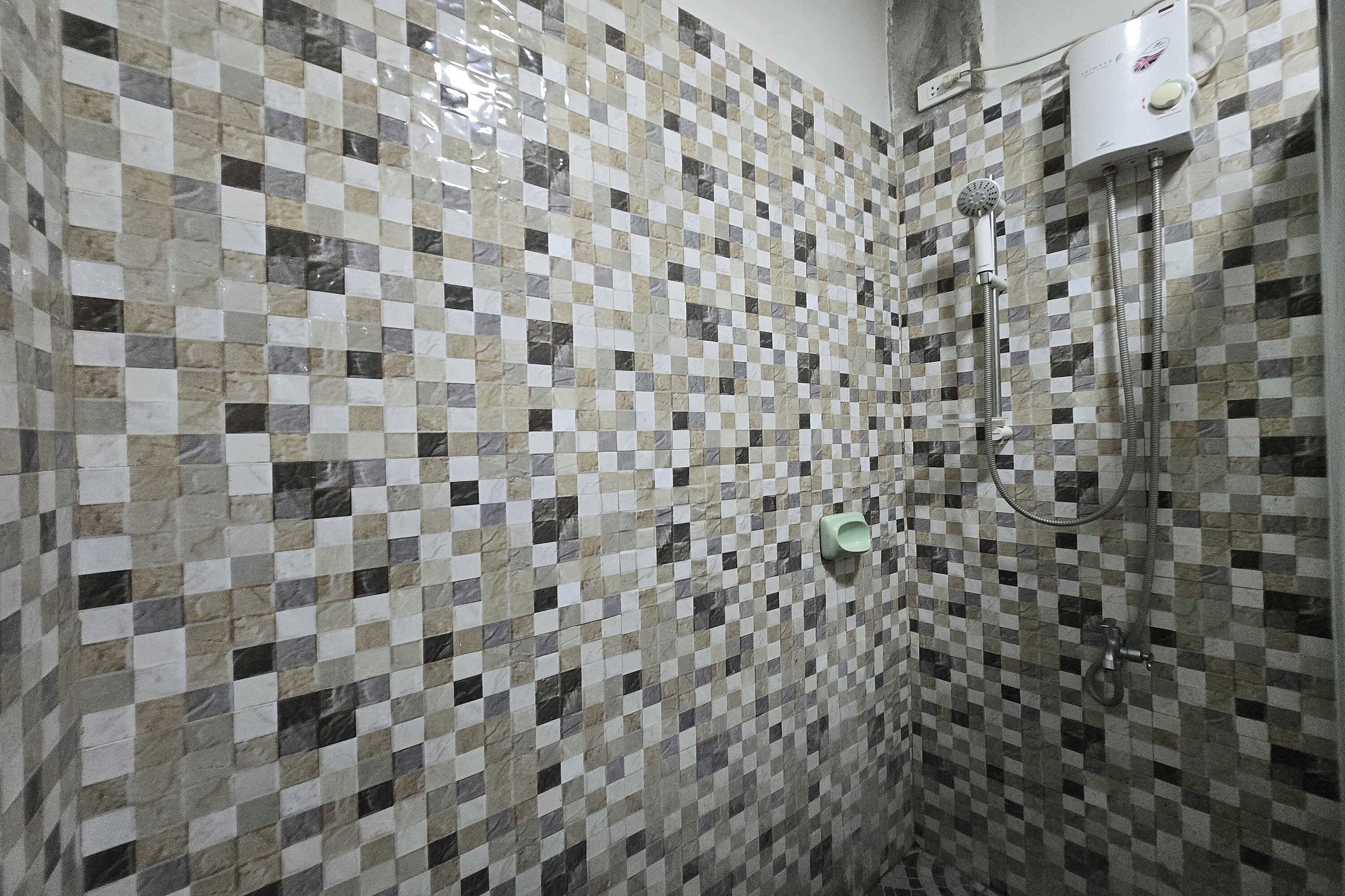 Un baño con pared de mosaicos a cuadros, un cabezal de ducha de mano y un grifo empotrado.