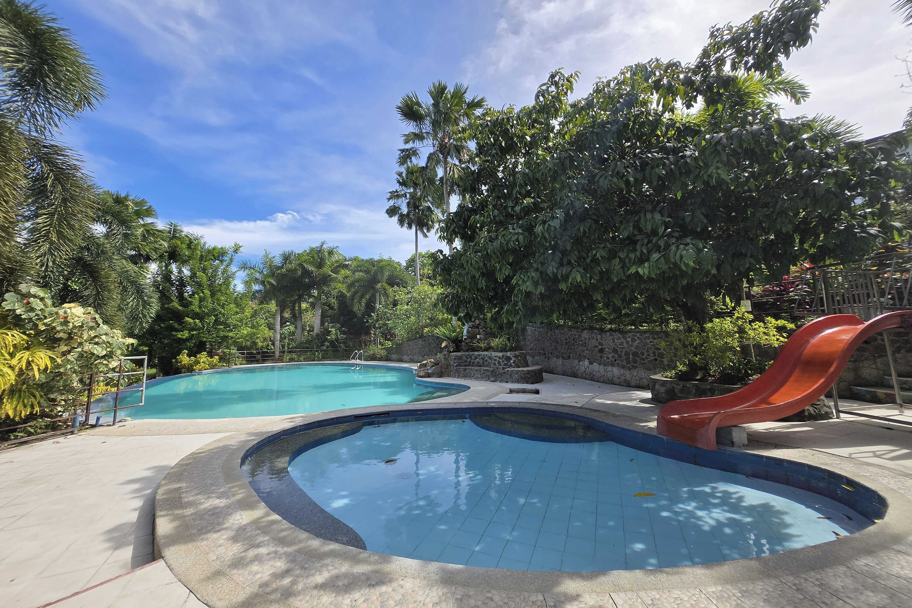 Une piscine avec un toboggan, entourée d’une végétation luxuriante et sous un ciel bleu azur.
