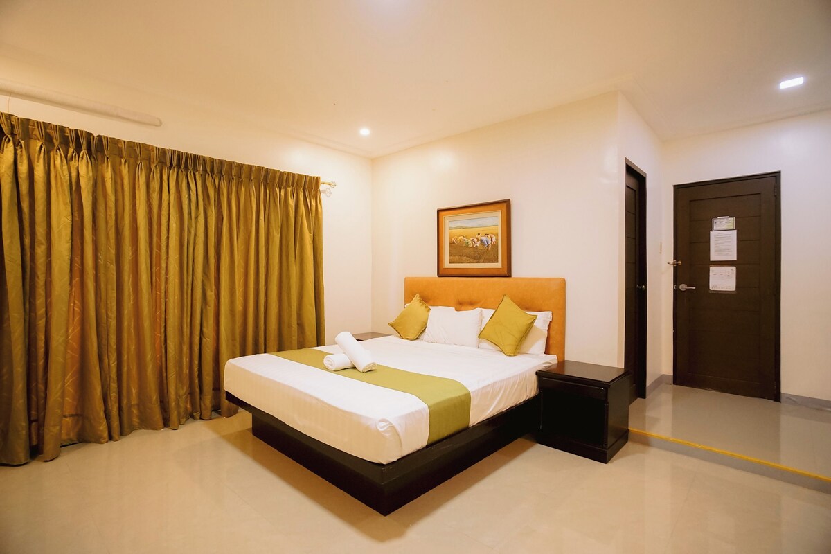 Una habitación de hotel con una cama, una mesita de noche, una puerta y una cortina.
