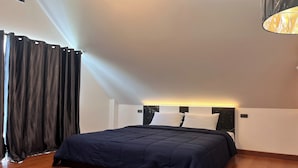 A bedroom with a bed, a headboard with built-in lighting, a window with curtains, and a wooden floor.