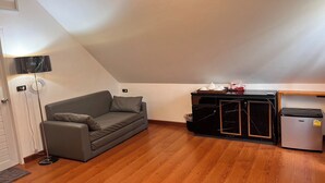 A compact living space with a grey sofa, a small black cabinet, and a compact refrigerator.