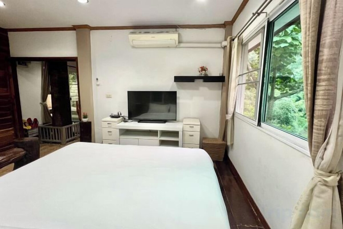 A hotel room with a bed, a TV, a small desk, and a window with curtains.