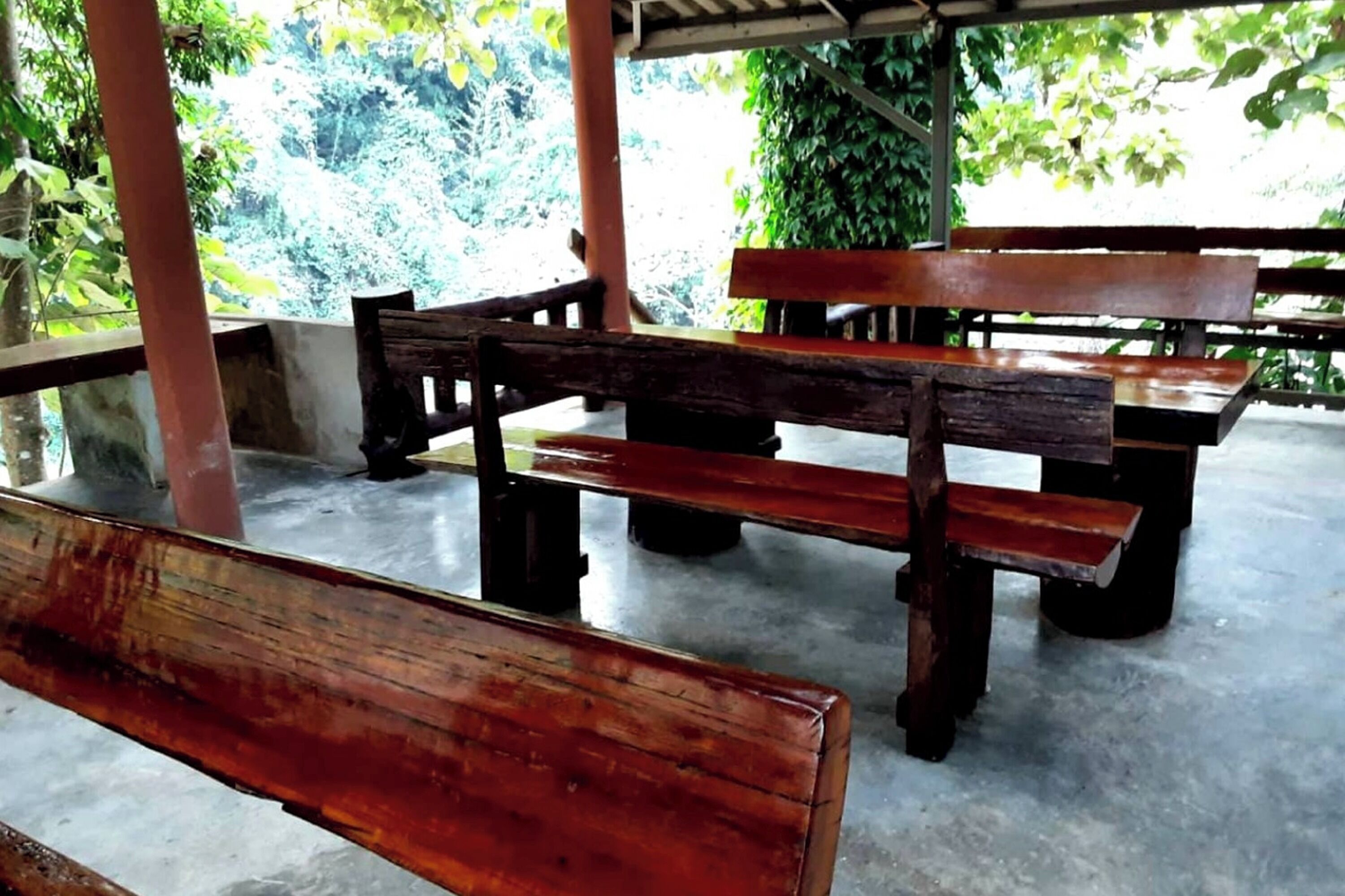 Een overdekt terras met houten banken en tafels.