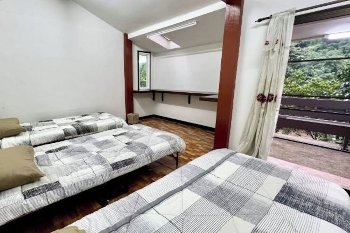 Una habitación con dos camas, un tragaluz, un ventanal con vistas a la vegetación y un balcón con barandilla.