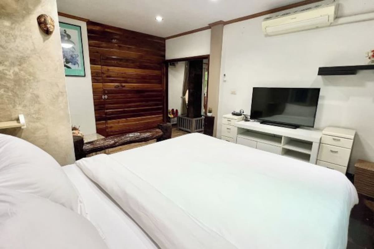 Habitación de hotel con una cama grande, televisión, pared decorativa de madera y escritorio con cajones.
