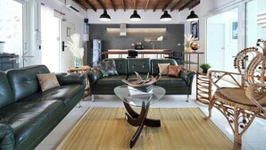 A modern living room with a glass coffee table, leather sofas, and a wooden ceiling.