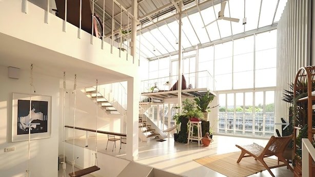 A spacious interior with a high ceiling, a staircase leading to an upper level, and a large window providing natural light.
