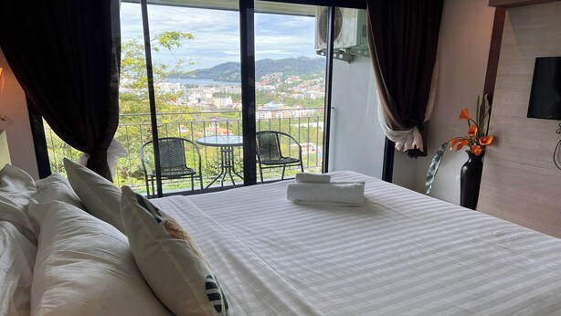 Habitación de hotel con una cama grande, vistas a la ciudad y un balcón con sillas.