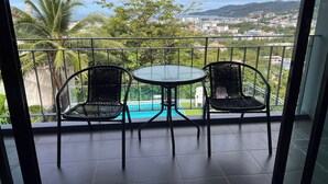 Un balcón con una mesa y sillas, con vista a una piscina y un paisaje urbano.