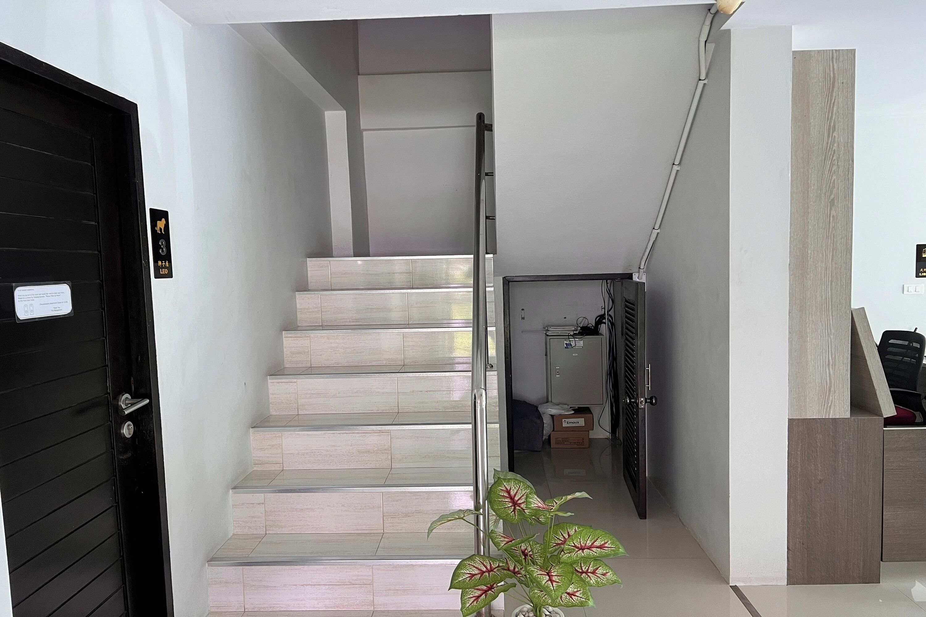 A modern staircase with a metal handrail, a black door with a sign, and a small plant.