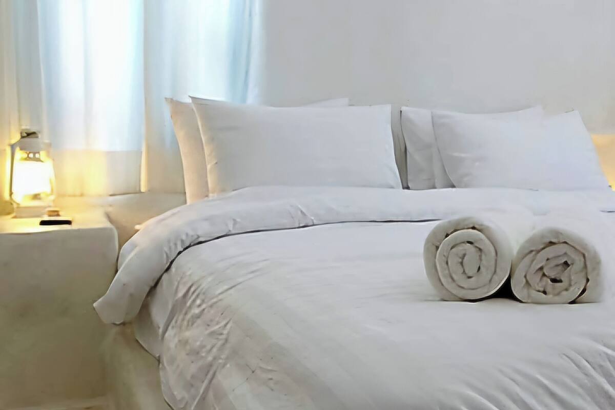Un lit bien fait, avec du linge de lit blanc et deux serviettes enroulées posées sur le côté.