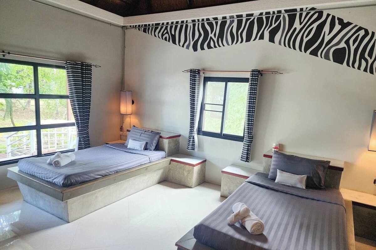 Une chambre d’hôtel avec deux lits, un motif à rayures zébrées sur un mur et de grandes fenêtres avec des rideaux.