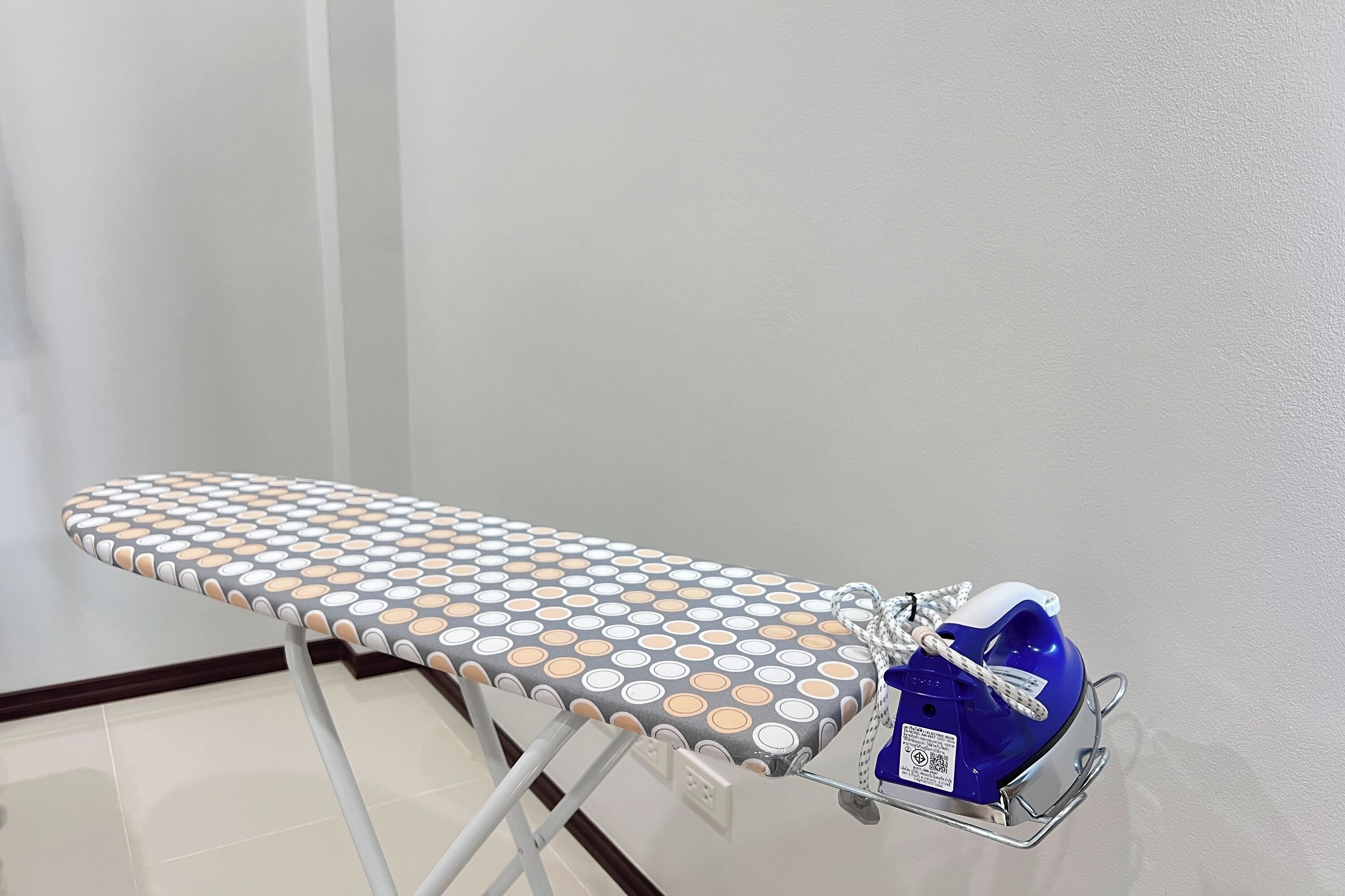 Una tabla de planchar con funda de lunares, un planchador azul y un soporte de metal.