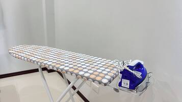 Una tabla de planchar con funda de lunares, un planchador azul y un soporte de metal.
