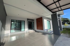 Une maison moderne dotée de grandes fenêtres, d’un patio couvert et d’un sol carrelé.