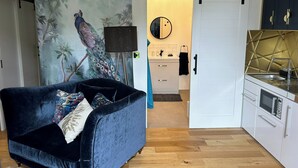 A modern living room with a dark blue sofa, a peacock mural, and a kitchen with white cabinets and a gold backsplash. - Charming Shropshire Ground Level Barn (Bridgnorth)