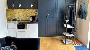 A compact kitchen with a microwave, coffee maker, and a sink. There is a dark-colored wardrobe with a geometric-patterned wall behind it. - Charming Shropshire Ground Level Barn (Bridgnorth)