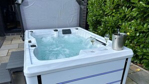 A hot tub with a metal container on top, surrounded by a hedge and a patio area. - Charming Shropshire Ground Level Barn (Bridgnorth)