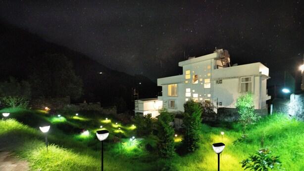 Une maison moderne dotée de nombreuses fenêtres et d’un jardin bien éclairé la nuit.