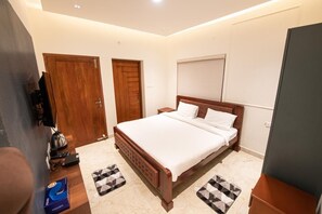 A bedroom with a large bed, two doors, a television, and a window with blinds. - Queen's Hotel Mount Garden Kodaikanal (Kodaikanal)
