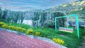 Un parc avec une balançoire verte, un banc rouge et jaune, et un mur de pierre recouvert de lierre.