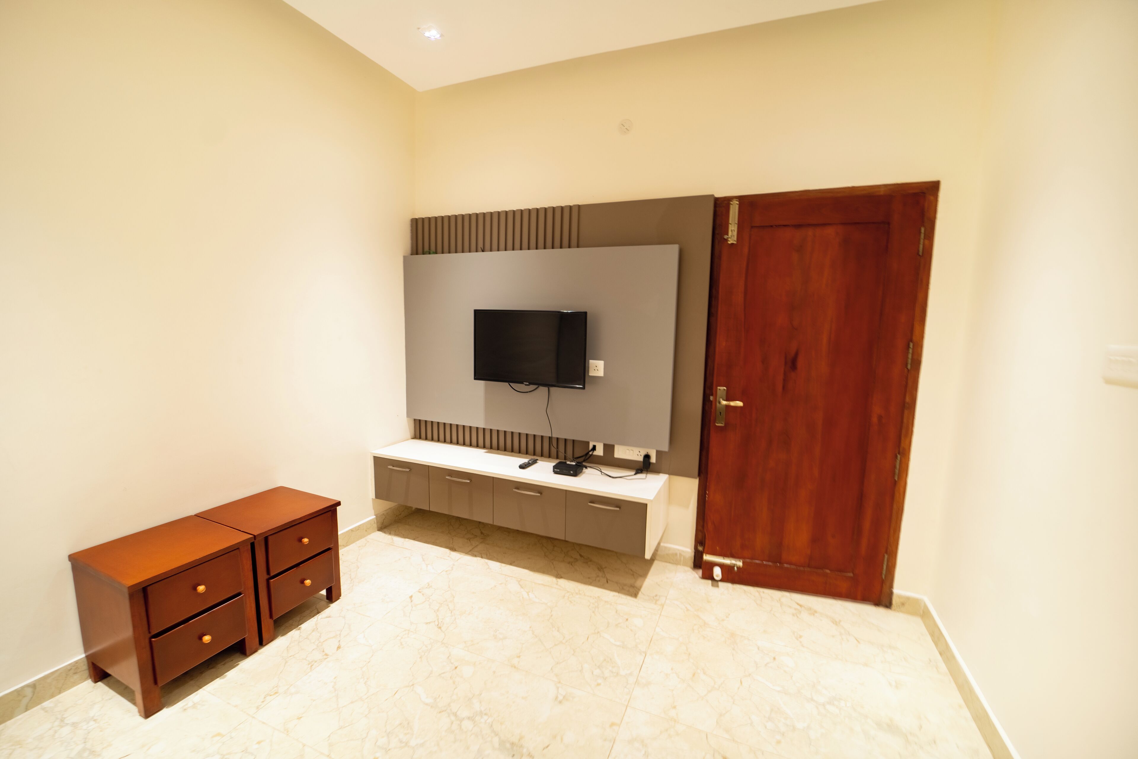 A room with a TV mounted on the wall, a wooden cabinet, and a door.