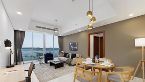 Ein modernes Hotelzimmer mit Essbereich, einer Sofagarnitur, einem großen Fenster mit Meerblick und einer Decke mit Einbaustrahlern.