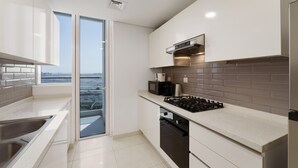Eine moderne Küche mit Gasherd, Mikrowelle und eingebautem Backofen. Weiße Schränke, ein großes Fenster und Blick auf die Stadt.