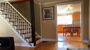 A staircase with white balusters and dark handrails, leading to a dining area with wooden chairs and a table.